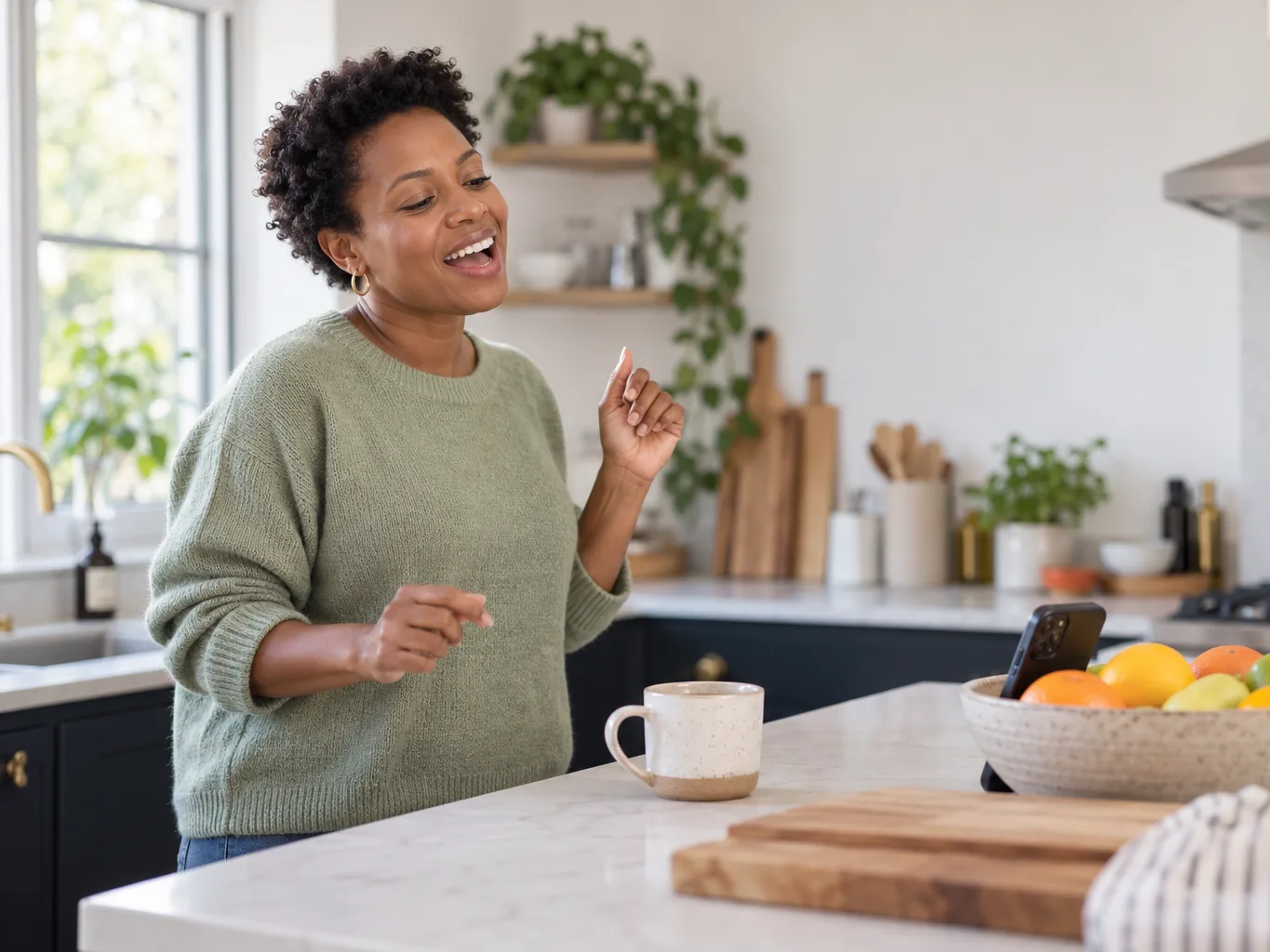 A woman in a green jumper singing along to her phone at a kitchen counter